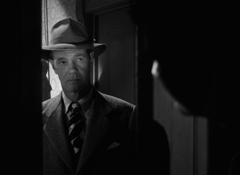 Movie still from “Crossfire” (1947), directed by Edward Dmytryk – A black and white photo of a man in a suit and hat; Close Up shot, Over the shoulder angle