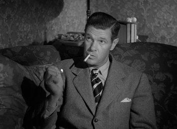 Movie still from “Crossfire” (1947), directed by Edward Dmytryk – A black and white photo of a man smoking a cigarette; Medium shot, Low angle