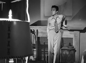 Movie still from “Crossfire” (1947), directed by Edward Dmytryk – A man in a suit and tie standing in front of a table; Medium shot, Low angle