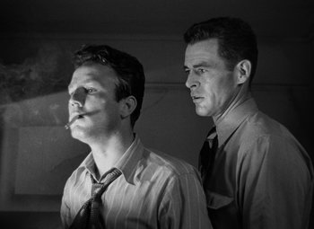 Movie still from “Crossfire” (1947), directed by Edward Dmytryk – Two men standing next to each other in a black and white photo; Medium shot, Low angle