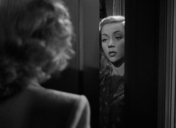 Movie still from “Crossfire” (1947), directed by Edward Dmytryk – A black and white photo of a woman looking in a mirror; Close Up shot, Over the shoulder angle