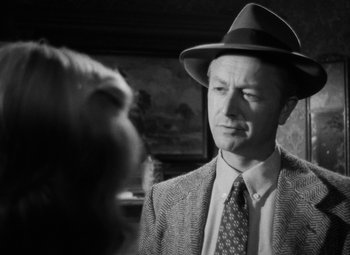 Movie still from “Crossfire” (1947), directed by Edward Dmytryk – A black and white photo of a man wearing a hat and a suit; Close Up shot, Over the shoulder angle