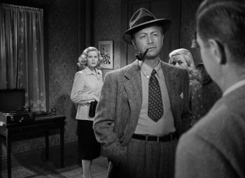 Movie still from “Crossfire” (1947), directed by Edward Dmytryk – A man in a hat smoking a pipe in front of two women; Medium shot, Over the shoulder angle