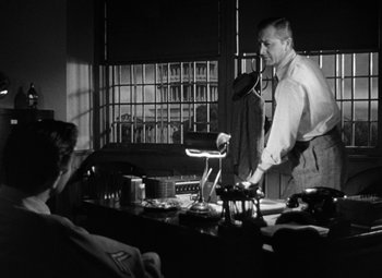 Movie still from “Crossfire” (1947), directed by Edward Dmytryk – A man standing in front of a table with a laptop; Medium shot, Low angle