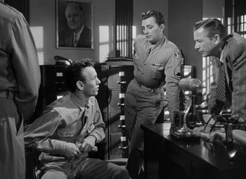 Movie still from “Crossfire” (1947), directed by Edward Dmytryk – A group of men standing around a table; Medium shot, Low angle