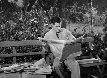 Movie still from “Crossfire” (1947), directed by Edward Dmytryk – A black and white photo of a man sitting on a park bench reading a newspaper; Medium shot, High angle