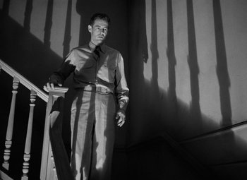 Movie still from “Crossfire” (1947), directed by Edward Dmytryk – A black and white photo of a man standing on stairs; Wide shot, Low angle