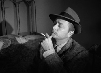Movie still from “Crossfire” (1947), directed by Edward Dmytryk – A black and white photo of a man smoking a cigarette; Close Up shot, High angle