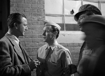Movie still from “Crossfire” (1947), directed by Edward Dmytryk – A group of men standing next to each other in front of a brick wall; Medium shot, Over the shoulder angle