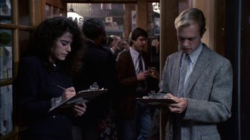A man and a woman looking down at a clipboard in front of other people
