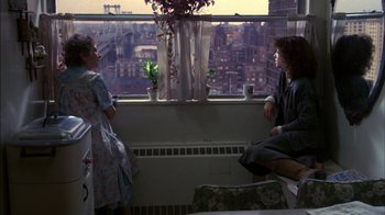 Movie still from “Crossing Delancey” (1988), directed by Joan Micklin Silver – Two people sitting in front of a window with a view of a city; Wide shot, High angle