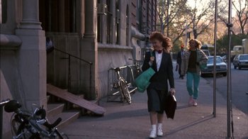 Movie still from “Crossing Delancey” (1988), directed by Joan Micklin Silver – A woman walking down a street holding a bag; Wide shot, Over the shoulder angle