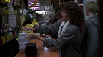 Movie still from “Crossing Delancey” (1988), directed by Joan Micklin Silver – A woman is holding a plate of hot dogs at a restaurant; Medium shot, Over the shoulder angle