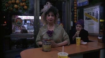 Movie still from “Crossing Delancey” (1988), directed by Joan Micklin Silver – A woman sitting at a table with a drink in front of her; Medium shot, Over the shoulder angle