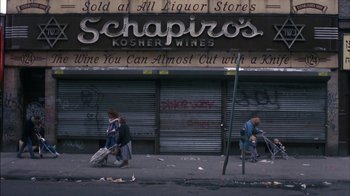 Movie still from “Crossing Delancey” (1988), directed by Joan Micklin Silver – Two people cleaning the sidewalk in front of a liquor store; Extreme Wide shot, High angle