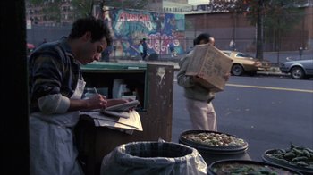 Movie still from “Crossing Delancey” (1988), directed by Joan Micklin Silver – A man writing on a piece of paper next to boxes of food; Medium shot, High angle
