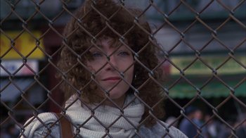 Movie still from “Crossing Delancey” (1988), directed by Joan Micklin Silver – A woman with curly brown hair looking through a chain link fence; Close Up shot, Low angle