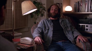 Movie still from “Crossing Delancey” (1988), directed by Joan Micklin Silver – A man sitting in a chair with a guitar in his lap; Medium shot, Low angle