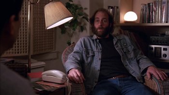 Movie still from “Crossing Delancey” (1988), directed by Joan Micklin Silver – A man sitting in a chair in front of a lamp; Medium shot, Low angle