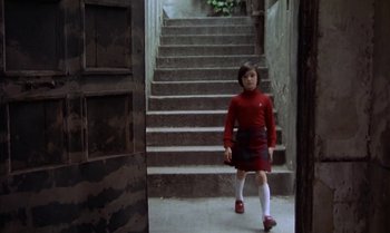 Movie still from “Cría Cuervos” (1976), directed by Carlos Saura – A girl in a red shirt and skirt walking down a set of stairs; Wide shot, Low angle