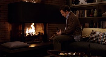 Movie still from “Cyrus” (2010), directed by Jay Duplass – A man sitting in front of a fire place; Wide shot, High angle