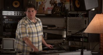 Movie still from “Cyrus” (2010), directed by Jay Duplass – A man standing in front of a bunch of electronic equipment; Medium shot, High angle