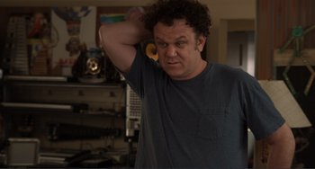 Movie still from “Cyrus” (2010), directed by Jay Duplass – A man in a blue t - shirt scratching his head with one hand; Medium shot, Over the shoulder angle