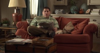 Movie still from “Cyrus” (2010), directed by Jay Duplass – A man sitting on a couch holding a newspaper; Medium shot, Over the shoulder angle