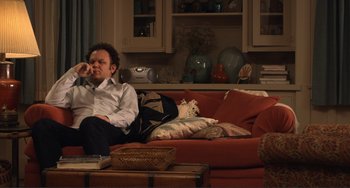 Movie still from “Cyrus” (2010), directed by Jay Duplass – A man sitting on top of a red couch in a living room; Medium shot, High angle