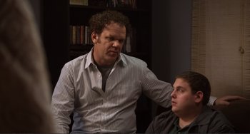 Movie still from “Cyrus” (2010), directed by Jay Duplass – A man standing next to another man in front of a book shelf; Medium shot, Over the shoulder angle