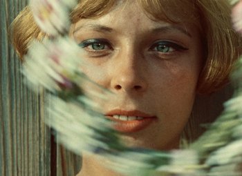 Movie still from “Daisies” (1966), directed by Vera Chytilová – A woman's face with flowers in the background; Close Up shot, Low angle
