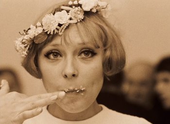 Movie still from “Daisies” (1966), directed by Vera Chytilová – A young woman wearing a flower crown eating something; Close Up shot, Low angle