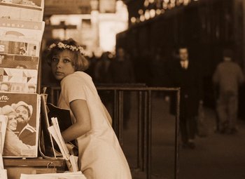 Movie still from “Daisies” (1966), directed by Vera Chytilová – A woman with a flower in her hair is leaning on a book shelf; Medium shot, High angle