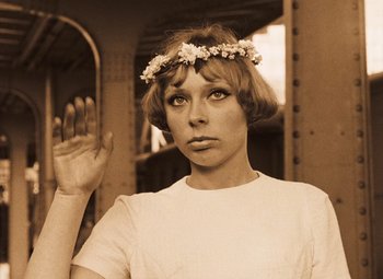 Movie still from “Daisies” (1966), directed by Vera Chytilová – A young woman wearing a flower crown is holding her hand up to her face; Close Up shot, Low angle