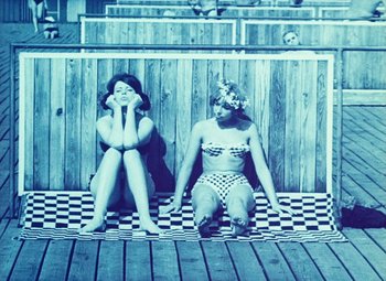 Movie still from “Daisies” (1966), directed by Vera Chytilová – Two women sitting on the ground in front of a wooden fence; Wide shot, High angle