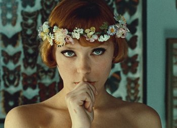 Movie still from “Daisies” (1966), directed by Vera Chytilová – A woman wearing a flower crown posing for a picture; Close Up shot, Low angle