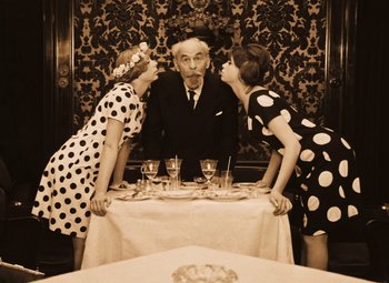 Movie still from “Daisies” (1966), directed by Vera Chytilová – A man sitting at a dinner table surrounded by two women; Medium shot, High angle
