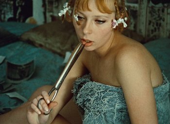 Movie still from “Daisies” (1966), directed by Vera Chytilová – A woman sitting on a bed holding a knife in her mouth; Close Up shot, High angle