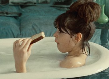 Movie still from “Daisies” (1966), directed by Vera Chytilová – A woman sitting in a bath tub holding a piece of bread; Medium shot, High angle