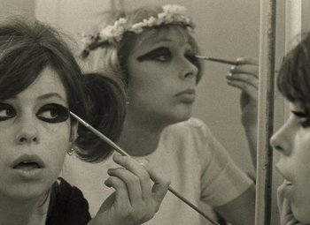Movie still from “Daisies” (1966), directed by Vera Chytilová – A woman putting makeup on another woman's face in a mirror; Close Up shot, Low angle