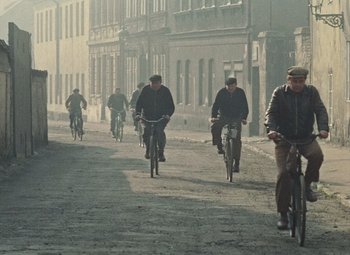 Movie still from “Daisies” (1966), directed by Vera Chytilová – A group of men riding bikes down a street; Wide shot, High angle
