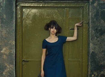 Movie still from “Daisies” (1966), directed by Vera Chytilová – A woman standing in front of a green door; Medium shot, High angle