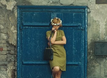 Movie still from “Daisies” (1966), directed by Vera Chytilová – A woman in a green dress standing in front of a blue door; Medium shot, High angle