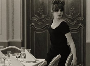 Movie still from “Daisies” (1966), directed by Vera Chytilová – A woman sitting at a dinner table in front of a wine glass; Medium shot, Over the shoulder angle