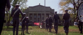 Movie still from “Damien: Omen II” (1978), directed by Mike Hodges – A group of men standing in front of a large building; Extreme Wide shot, Low angle