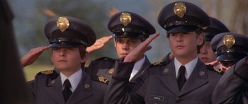 Movie still from “Damien: Omen II” (1978), directed by Mike Hodges – A group of men in uniform saluting in front of trees; Medium shot, Low angle