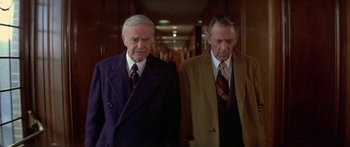 Movie still from “Damien: Omen II” (1978), directed by Mike Hodges – Two older men in suits and ties in a hallway; Medium shot, Low angle