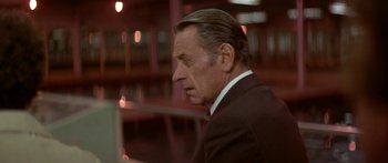 Movie still from “Damien: Omen II” (1978), directed by Mike Hodges – An older man wearing a suit and red tie; Close Up shot, Over the shoulder angle