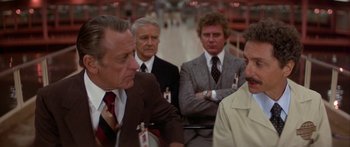 Movie still from “Damien: Omen II” (1978), directed by Mike Hodges – A group of men standing next to each other in a room; Medium shot, Over the shoulder angle