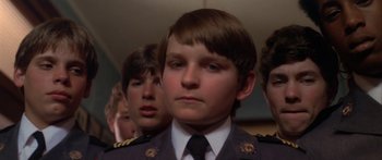 Movie still from “Damien: Omen II” (1978), directed by Mike Hodges – A group of young men standing next to each other in uniforms; Close Up shot, Low angle